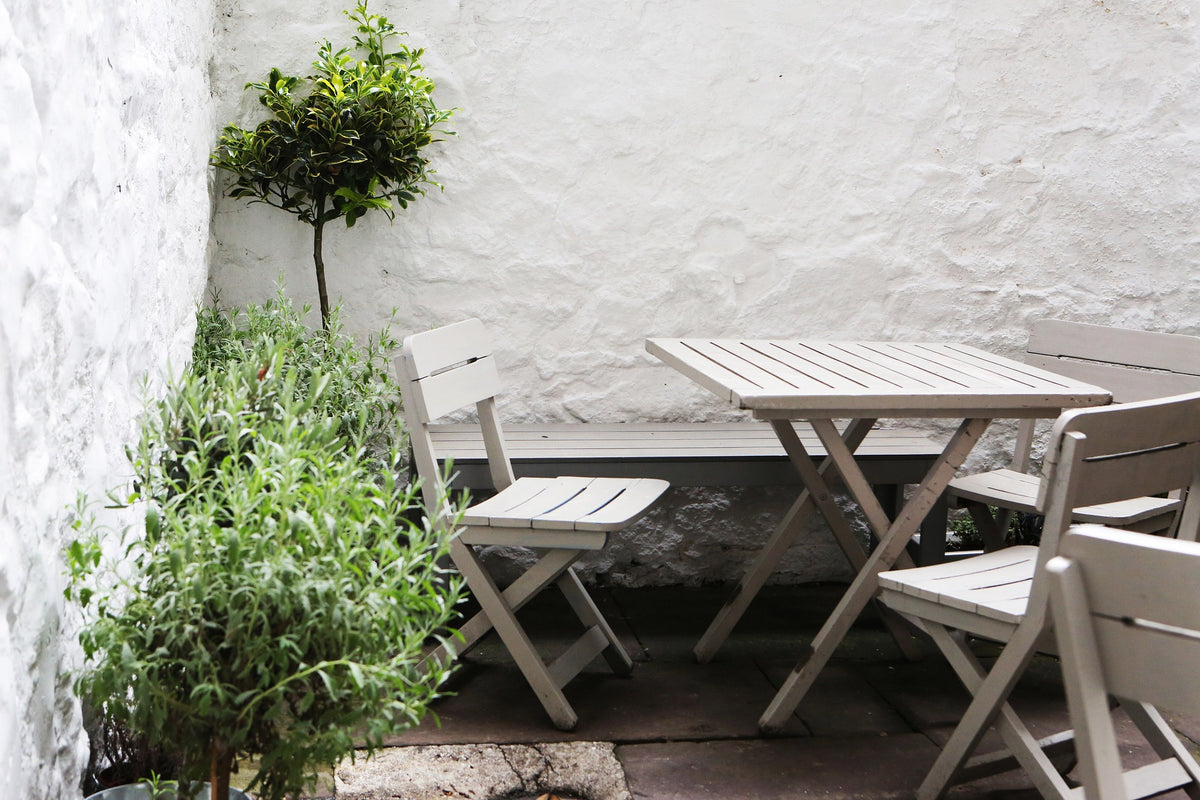 Gemütliche Bambusterrasse in einem kleinen Innenhof mit Gartenmöbeln und mediterraner Bepflanzung an weißer Steinwand.